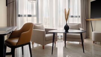 Una sala de estar moderna con un sofá, dos sillones, una mesa redonda y un televisor montado en la pared.