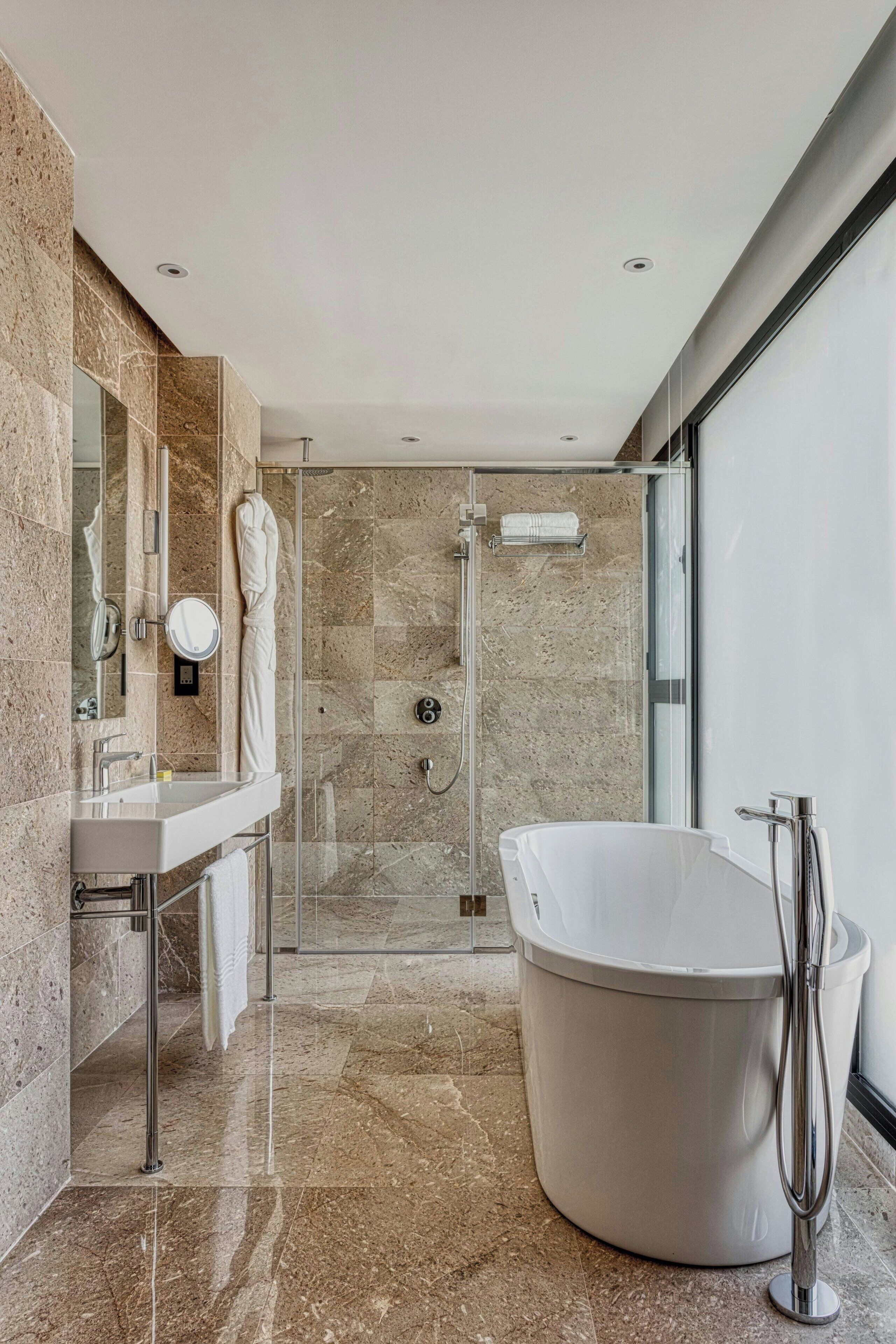 Un baño moderno con una bañera independiente, ducha con mampara de vidrio y tocador con espejo y perchero.