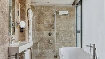 Un baño moderno con una bañera independiente, ducha con mampara de vidrio y tocador con espejo y perchero.