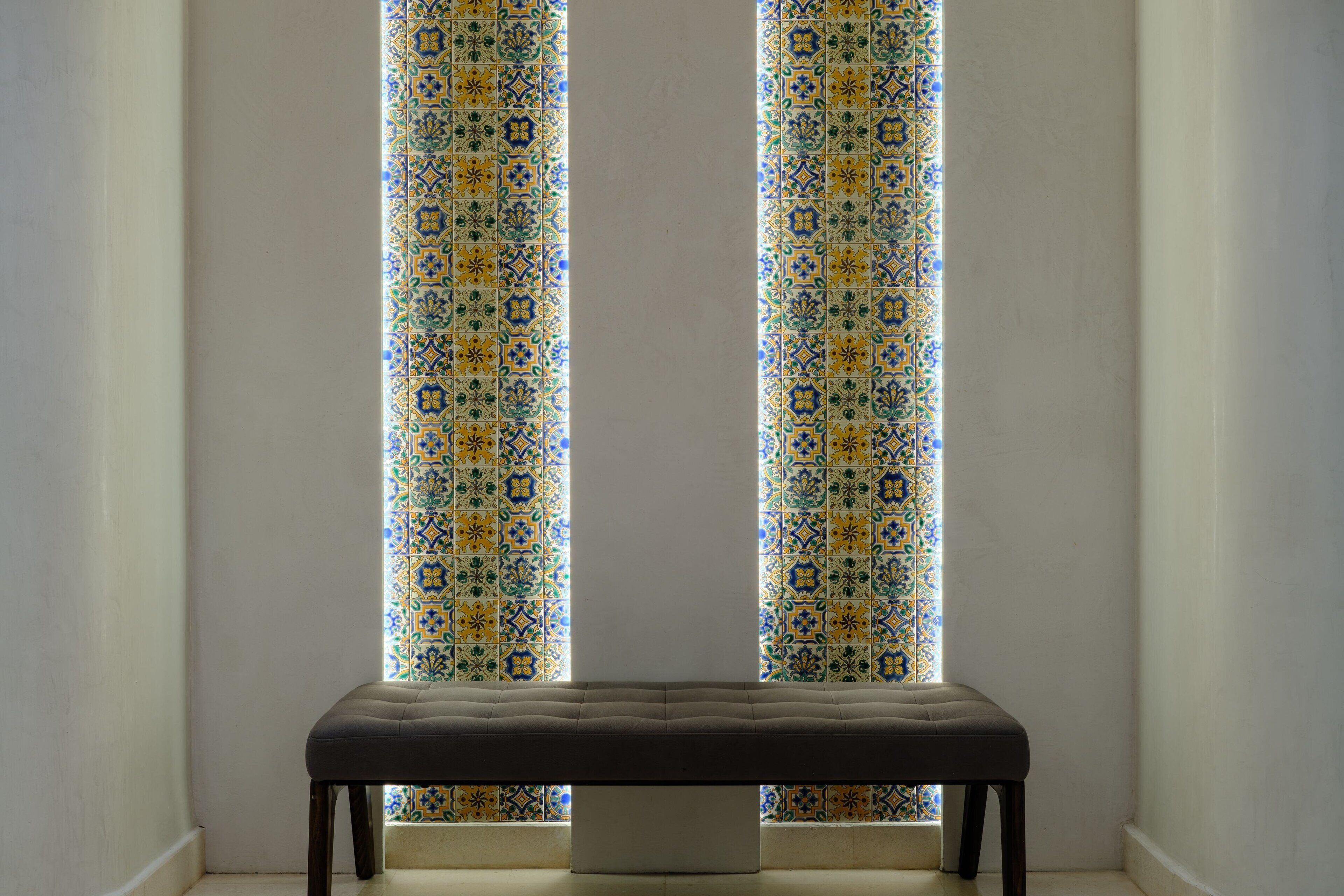A bench in a corner with a patterned window behind it.