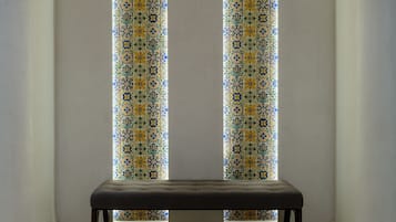 A bench in a corner with a patterned window behind it.