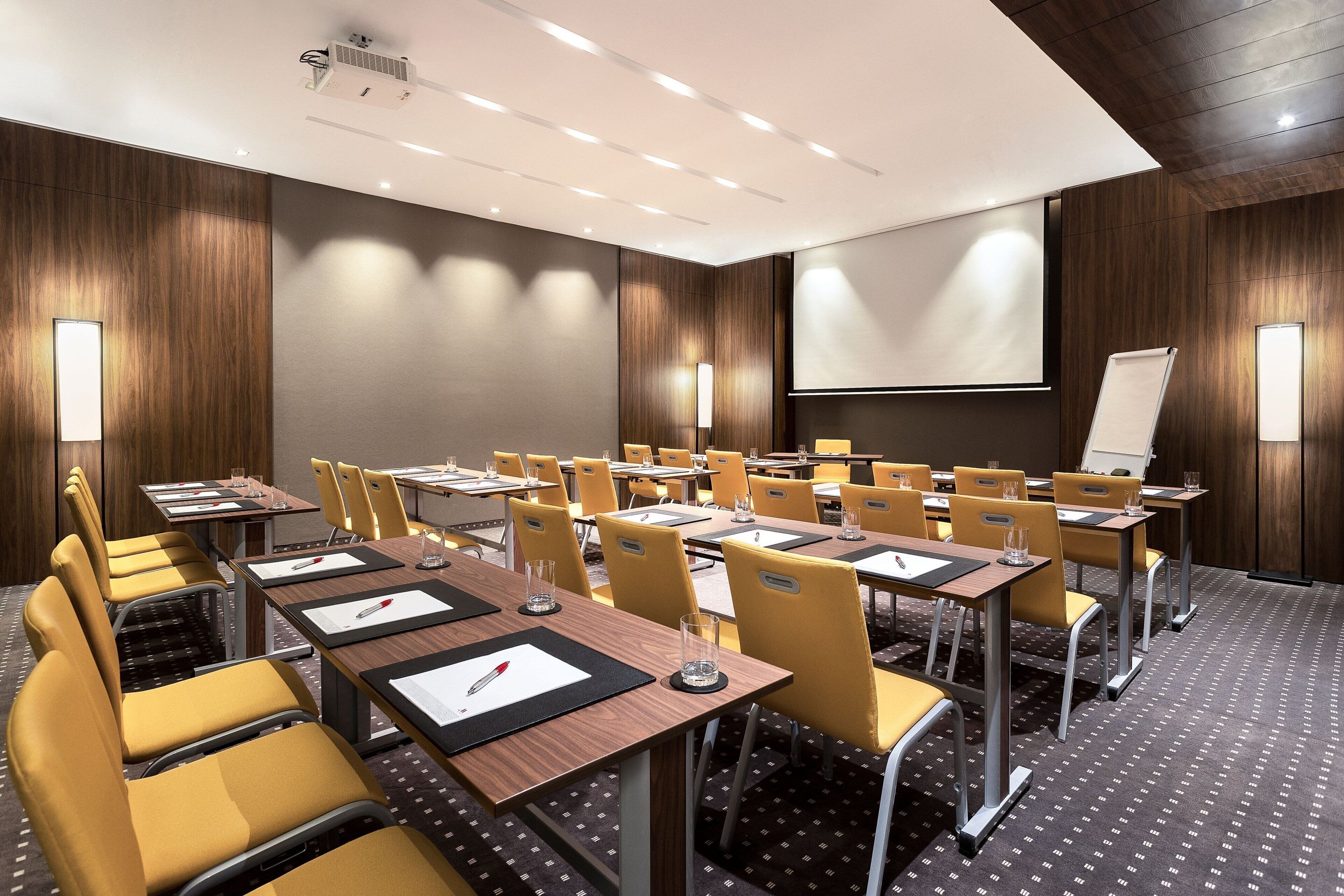 A conference room with multiple tables and chairs, equipped with projectors and screens.