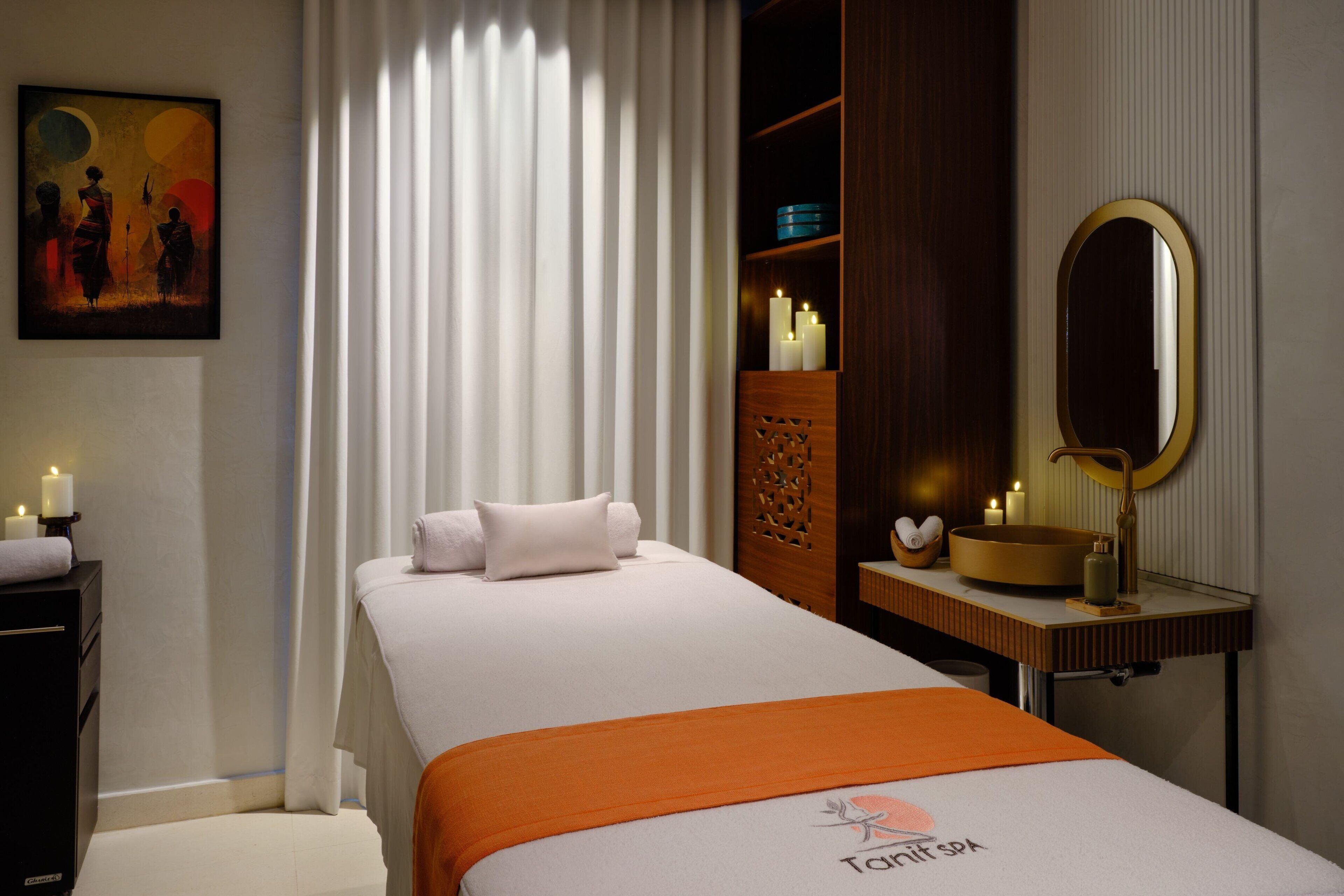 Ein Hotelzimmer mit Bett, Nachttisch mit Kerzen, Spiegel und einem Gemälde an der Wand.