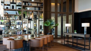 A modern interior with a wooden bar area, leather bar stools, and a large bookshelf filled with books and decorative items. - Tunis Marriott Hotel (Tunis)