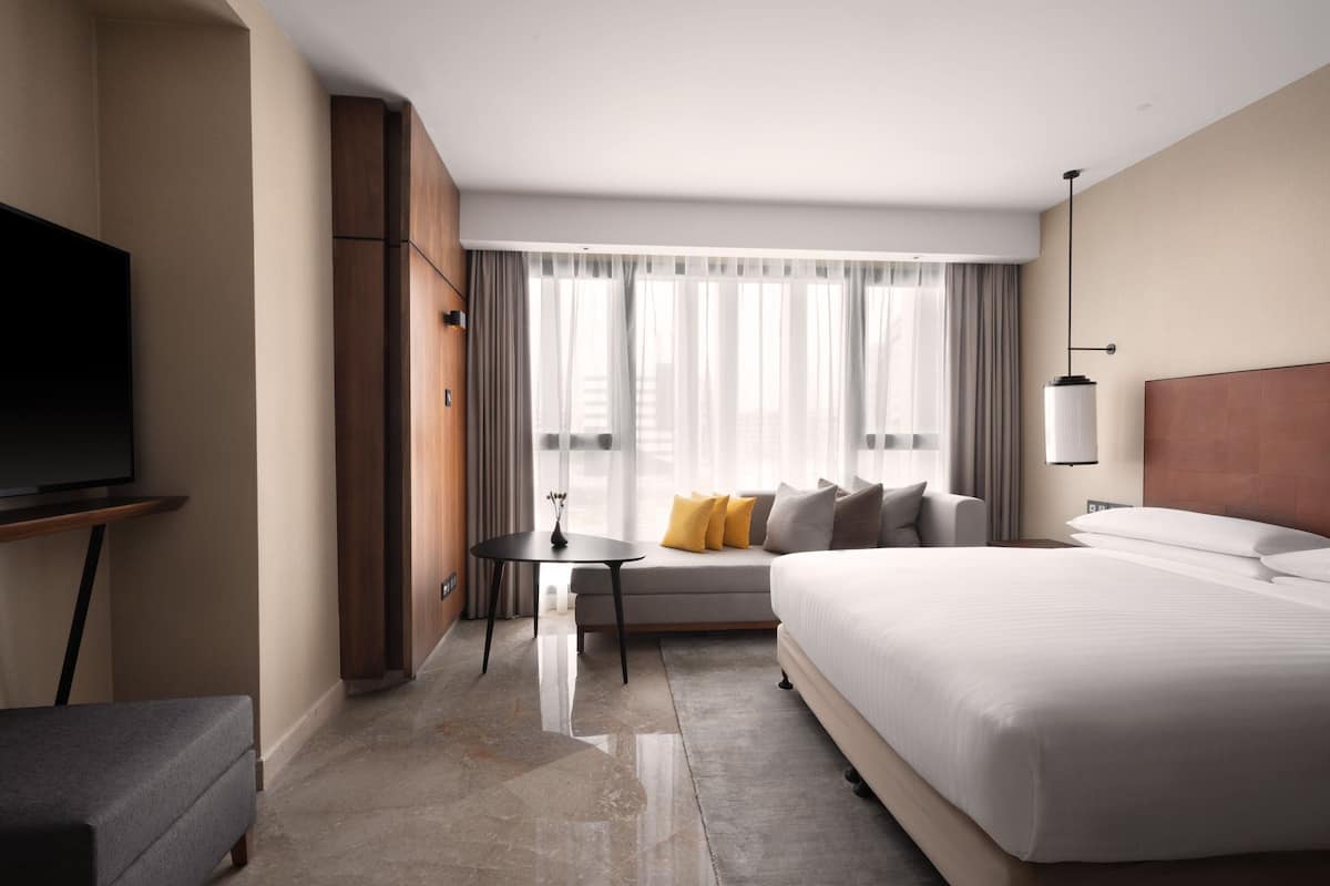 A modern hotel room with a large bed, a sofa, a TV, and a window with curtains.
