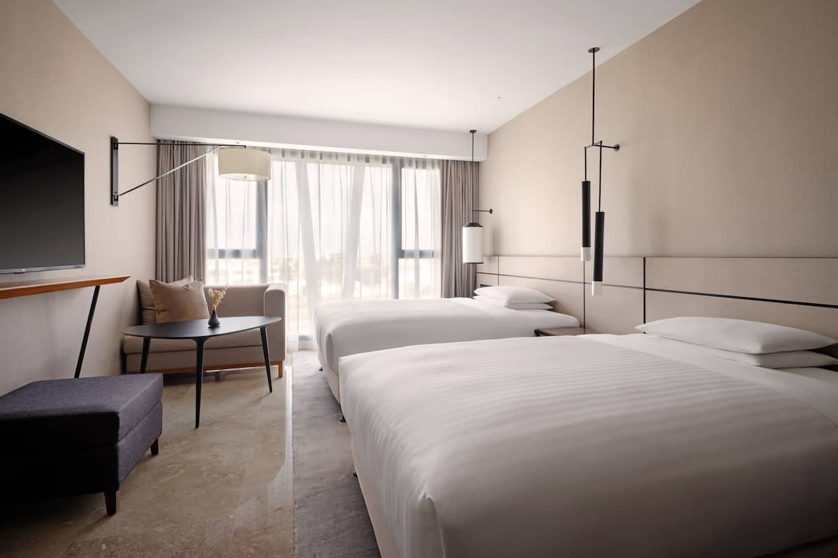 A hotel room with two beds, a TV, a desk, and a chair.