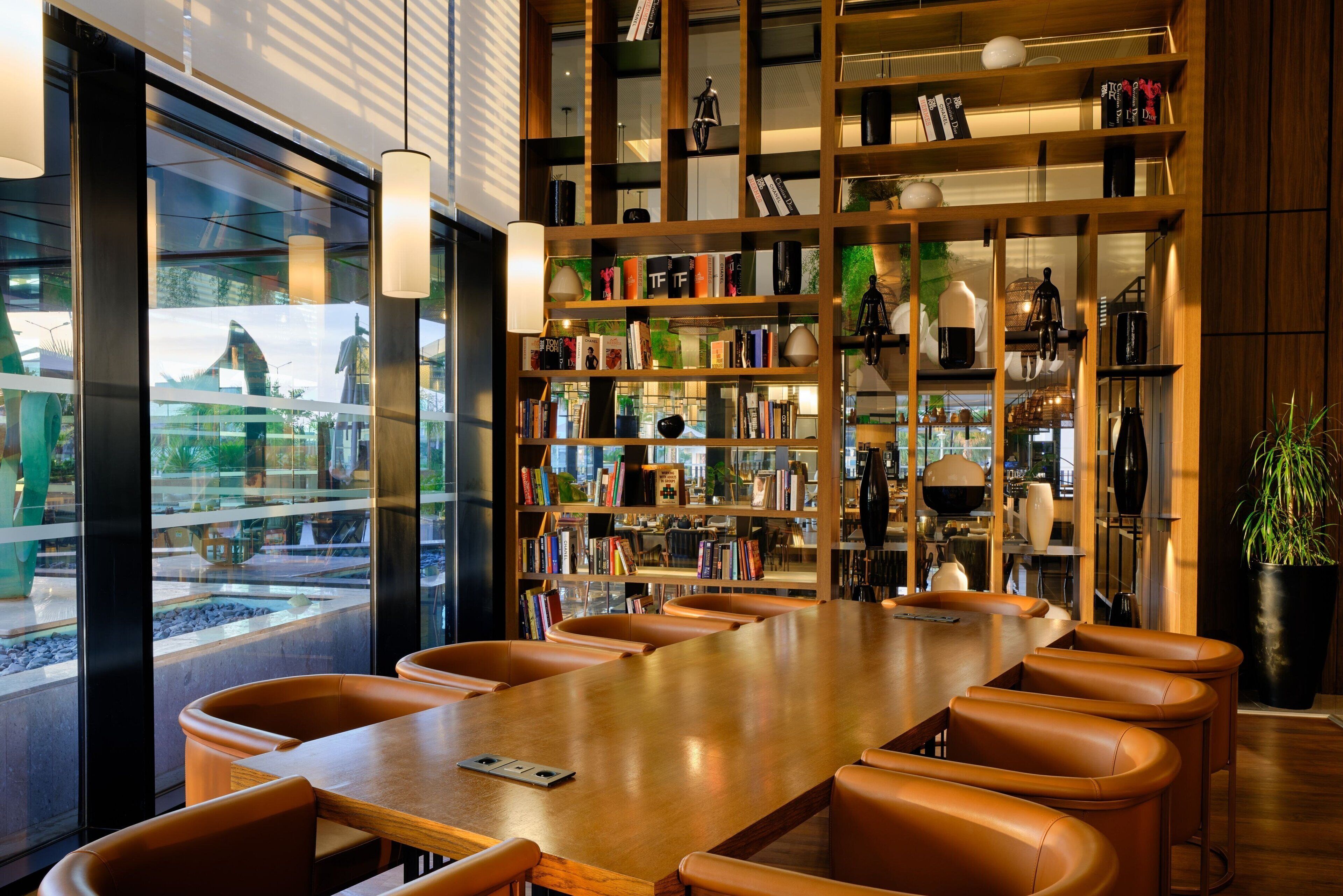 Una sala conferenze moderna con un lungo tavolo di legno, poltrone in pelle e una libreria piena di libri e oggetti decorativi.