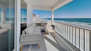 Un balcon avec un canapé et une table, donnant sur une plage et l’océan.