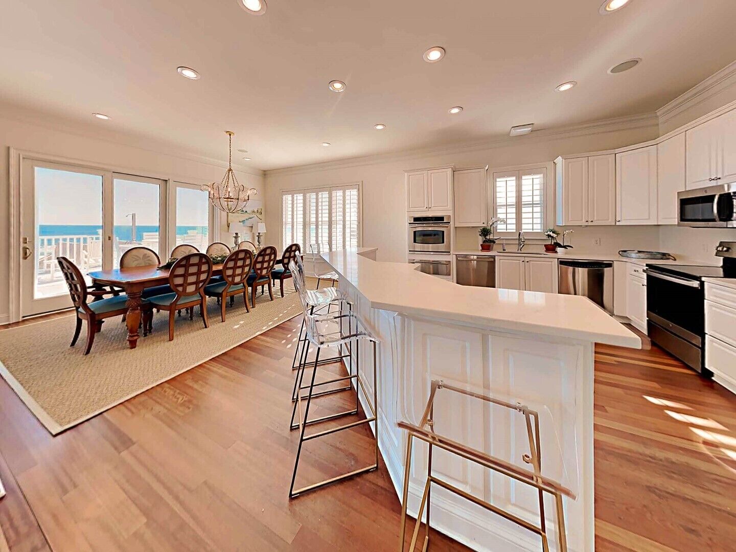 A modern kitchen with white cabinetry, a central island, and a dining area with wooden chairs and a chandelier.