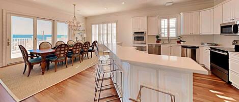 A modern kitchen with white cabinetry, a central island, and a dining area with wooden chairs and a chandelier.