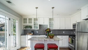 Une cuisine moderne avec des meubles blancs, un îlot en marbre, des appareils électroménagers en acier inoxydable et une grande fenêtre qui laisse entrer la lumière naturelle.