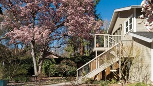 Un immeuble résidentiel doté d’un escalier à deux niveaux, d’un grand arbre en fleurs et d’un jardin bien entretenu.