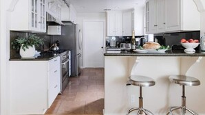 A modern kitchen with white cabinetry, a stainless steel refrigerator, a gas stove, and a bar area with stools. - Stargaze your evenings away in the private backyard Hot Tub. (Chico)