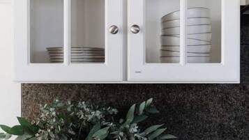 A kitchen with white cabinets, a granite countertop, a potted plant, and a tray with kitchen utensils.