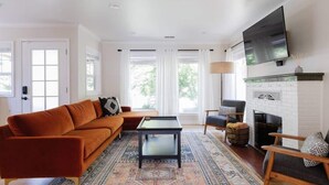 A living room with a sofa, coffee table, armchair, fireplace, and a TV mounted on the wall. - Stargaze your evenings away in the private backyard Hot Tub. (Chico)