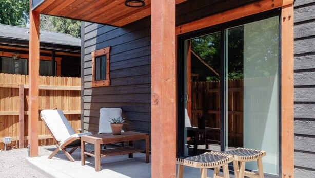 Eine Holzterrasse mit Stuhl, Tisch und einer Topfpflanze, sowie eine Glastür zu einem überdachten Bereich.