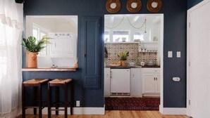 A modern kitchen with white cabinets, a wooden countertop, and a red rug. There are two stools and a potted plant. - | The Jungle Bungalow | Downtown Chico | (Chico)