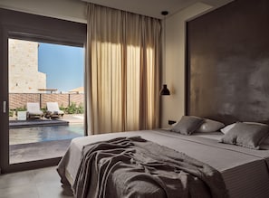 Ein Schlafzimmer mit einem großen Bett, Blick auf einen Pool und einem dahinterliegenden Steinhaus.