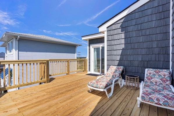 A wooden deck with two white lounge chairs and a wicker basket.