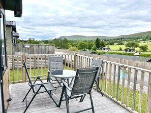 A balcony with a table and chairs, overlooking a scenic landscape with hills and a wooden fence.
