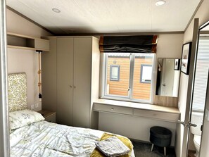A compact bedroom with a bed, a wardrobe, a small desk, and a window with a view of a building.