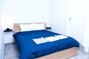 A neatly made bed with a blue bedspread and white pillows, a bedside table with a lamp, and a door to the right. - Veranda Apt close to Monastiraki - 1 (Athens)