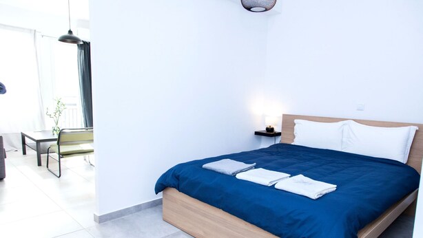 A modern hotel room with a neatly made bed, a bedside table with a lamp, and a view of the outdoor area. - Veranda Apt close to Monastiraki - 1 (Athens)