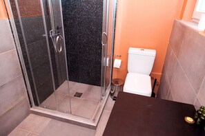 A bathroom with a glass shower enclosure, a white toilet, and a dark countertop. - Veranda Apt close to Monastiraki - 1 (Athens)