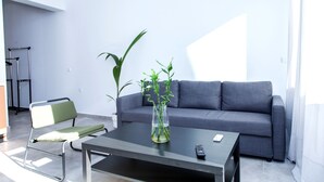 A modern living room with a grey sofa, a green chair, a coffee table, and a vase with plants. - Veranda Apt close to Monastiraki - 1 (Athens)
