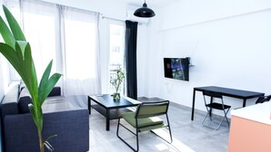 A modern living room with a sofa, a dining table, a chair, a potted plant, and a TV mounted on the wall. - Veranda Apt close to Monastiraki - 1 (Athens)