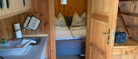 Una cabaña de madera compacta con kitchenette, una cama con ropa de cama estampada y un pequeño armario.