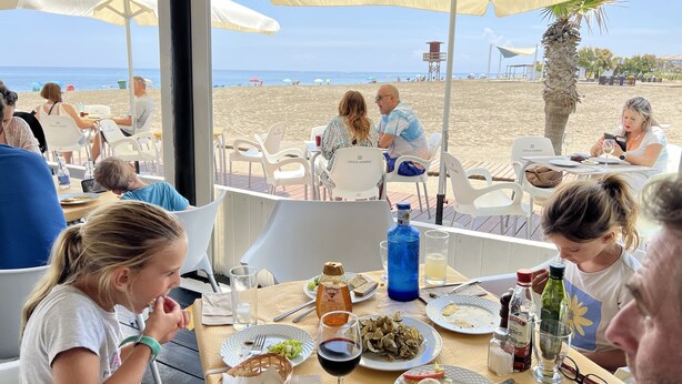 An outdoor dining area with tables and chairs, overlooking a beach. - Beautiful modern apartment 1 min from beach (Marina de Casares)