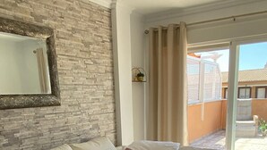 A bedroom with a large bed, a brick accent wall, a mirror, and a view of the outside. - Beautiful modern apartment 1 min from beach (Marina de Casares)