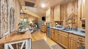L’intérieur d’un chalet en bois comprend une cuisine équipée de meubles en bois, d’un plan de travail en marbre et d’un coin repas avec une table et des chaises.