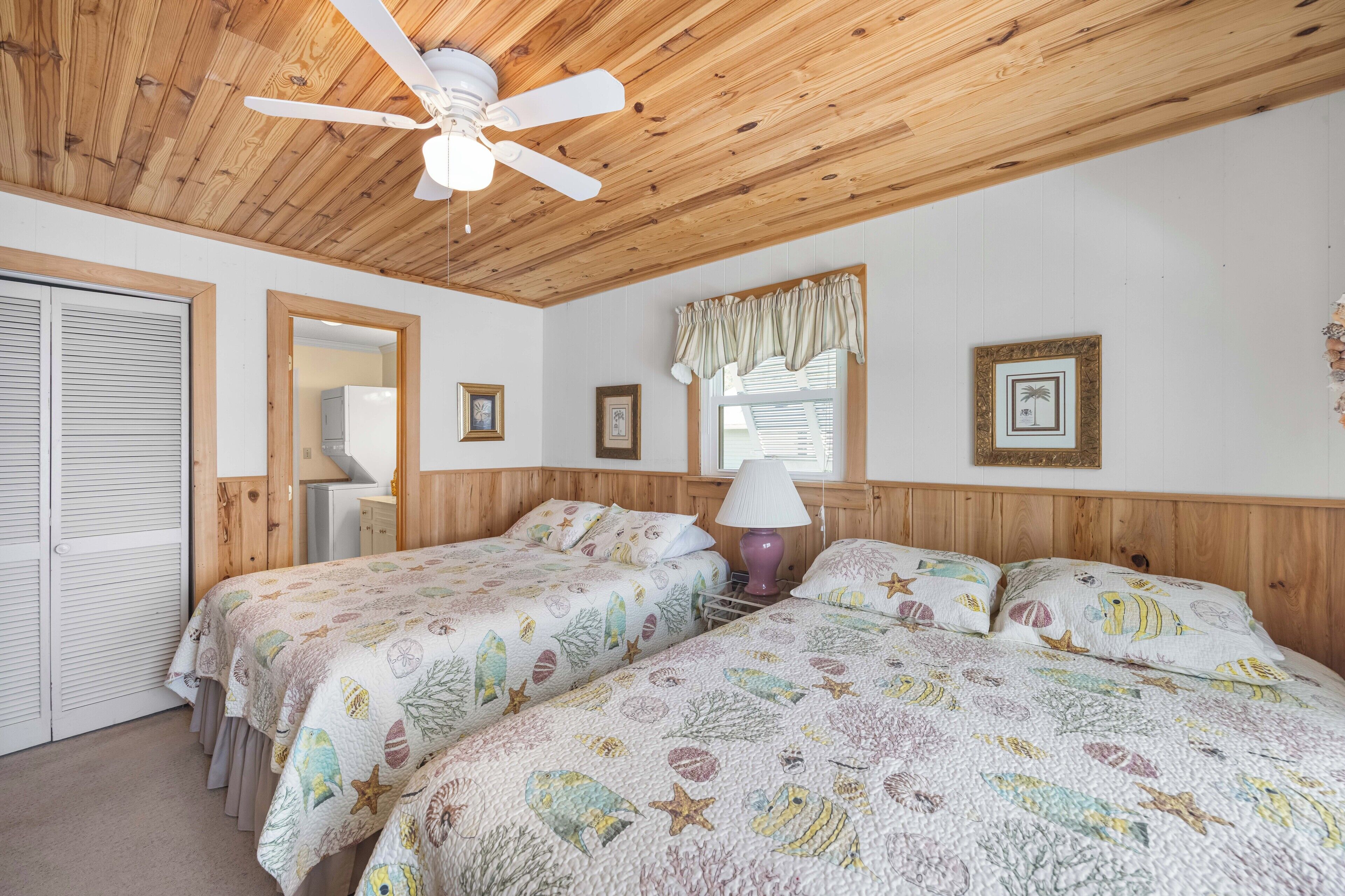 A bedroom with two beds, wooden ceiling, and a ceiling fan.