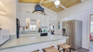 A kitchen with a large island, white cabinets, a stainless steel refrigerator, and a ceiling fan.