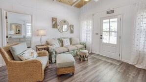 A cozy living room with a wicker chair, a patterned sofa, and a matching ottoman. A ceiling fan and a mirror are visible, along with a door leading outside.