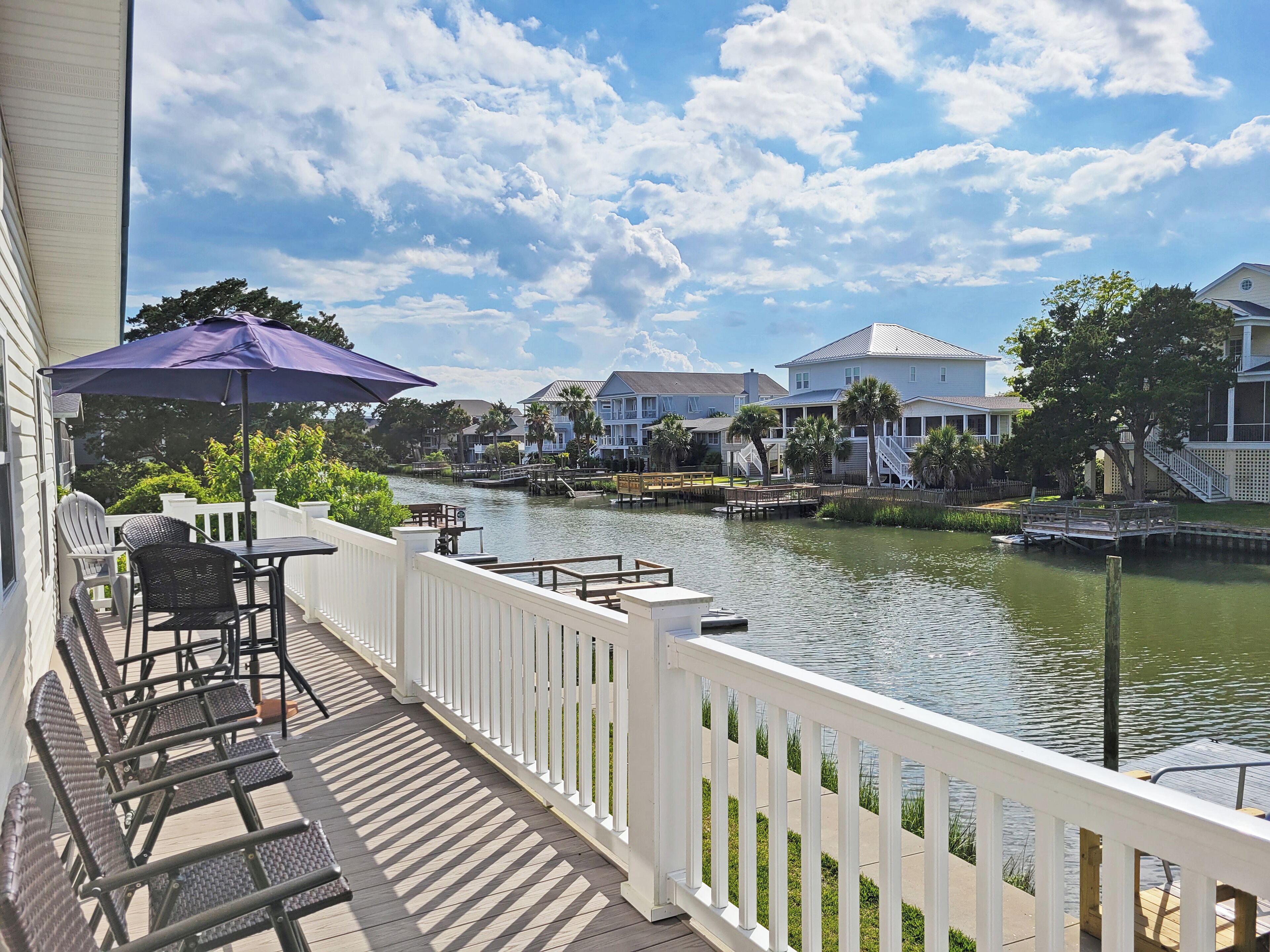 A waterfront balcony with a view of a river, white railings, and a table with chairs.
