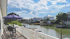 A waterfront balcony with a view of a river, white railings, and a table with chairs.