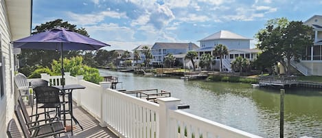 A waterfront balcony with a view of a river, white railings, and a table with chairs.