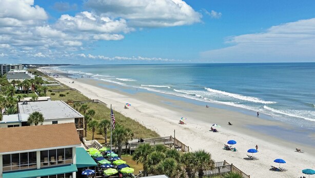 A beach with umbrellas, a flag, and a view of the ocean.