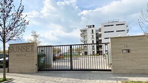 A gated entrance to a modern apartment complex named 'SUNSET SIÖFOK' with a paved driveway and a clear sky. - Sunset Beach Apartment directly on the beach high-quality furnishings pool garden WLAN (Siófok)