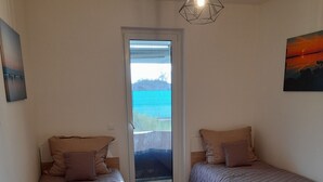 A bedroom with two single beds, a large window, and a view of the outdoors. - Sunset Beach Apartment directly on the beach high-quality furnishings pool garden WLAN (Siófok)