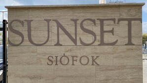 A sign with the word "SUNSET" and the name "SIOFOK" on a stone wall. - Sunset Beach Apartment directly on the beach high-quality furnishings pool garden WLAN (Siófok)