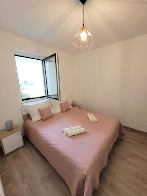 A bedroom with a large bed, a window, a bedside table, and a hanging light fixture.