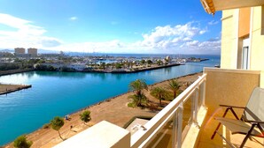 Un balcón con vistas a un puerto deportivo, cielo despejado y montañas a lo lejos.