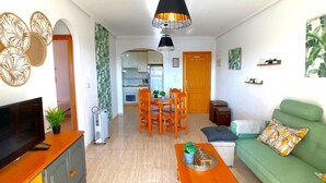 Una sala de estar con televisor, sofá, mesa de centro y un comedor con sillas y una mesa.