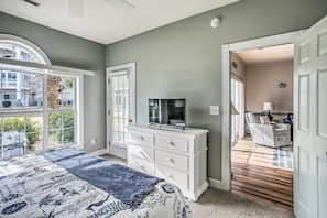 Relax in this serene bedroom with a large bed, flat-screen TV, and a door leading to a separate room with a sofa.