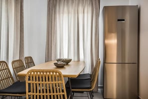 Ein Essbereich mit Holztisch, Korbstühlen und einem Edelstahlkühlschrank.