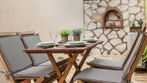 Una terrazza esterna con un muro in pietra, un forno a mattoni e poltrone imbottite a righe.